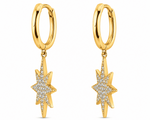 A pair of gold huggie hoop earrings with dangling starburst charms paved with clear stones, shown on a plain white background.