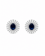 A pair of silver-toned stud earrings featuring oval-cut dark blue sapphires surrounded by radiating rows of small clear stones, set against a plain white background.