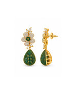 A pair of gold and green drop earrings on a plain white background. One earring is shown from the front, featuring a flower-shaped top set with small clear stones and a green center, with a teardrop-shaped drop below covered in green stones.