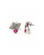 A pair of silver-toned floral stud earrings featuring white pearls, pavé-set clear stones, and a heart-shaped pink gemstone, shown on a plain white background.
