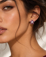 A close-up of a woman's ear wearing a small star-shaped stud earring with a white pearl center and purple gemstone points.